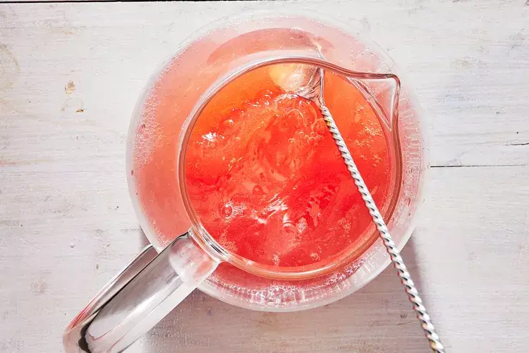 A chilled glass of Peach Sangria garnished with fresh peach slices and mint, served with a straw on a sunny day. 