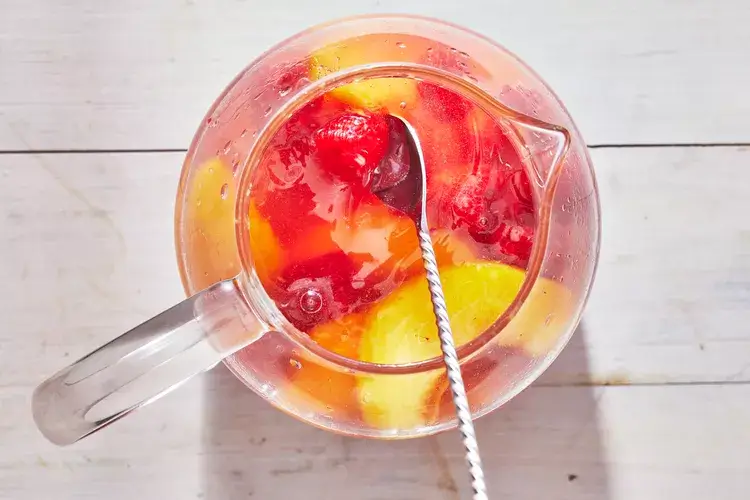 A refreshing pitcher of Peach Sangria with slices of peaches, citrus, and tropical fruit floating in white wine.