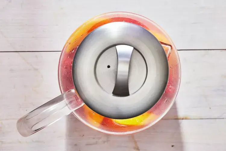 A pitcher of Peach Sangria with colorful fruit slices and ice, served on a sunny patio for summer relaxation.