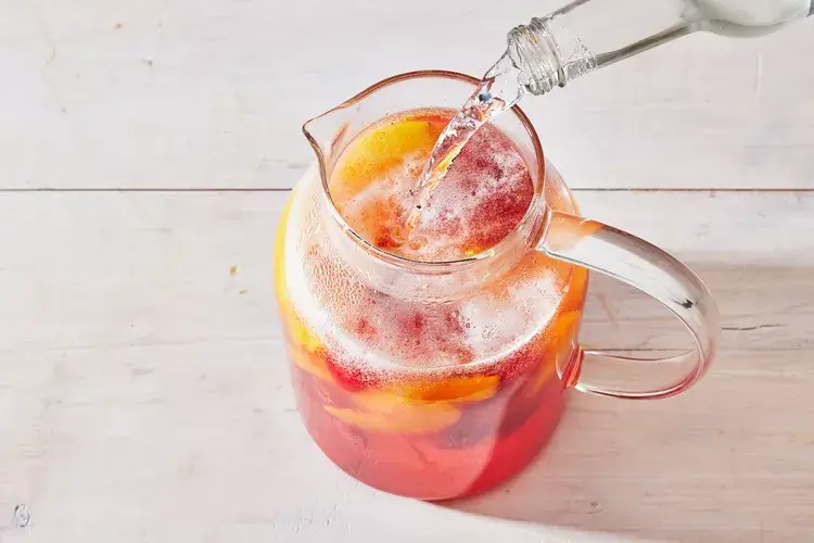 Glasses of Peach Sangria garnished with fresh peach slices and mint, served with a splash of club soda for added fizz.