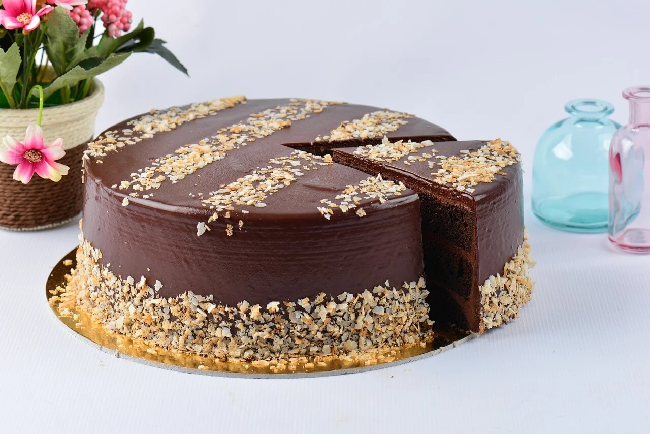 A rich and decadent Ferrero Ferrero Rocher Dessert with a glossy ganache topping, garnished with crushed hazelnuts and a slice cut out, revealing a moist interior.