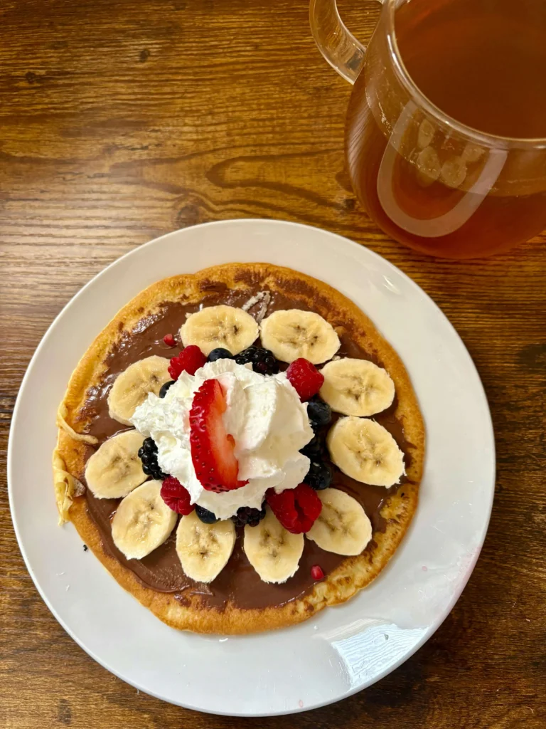 Delicious berry pancakes served with fresh fruit and warm honey on a white plate