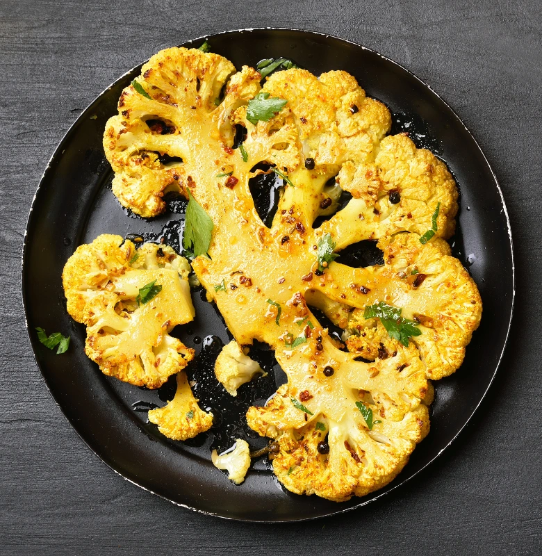 Roasted cauliflower steak with herbs on a black ceramic plate.