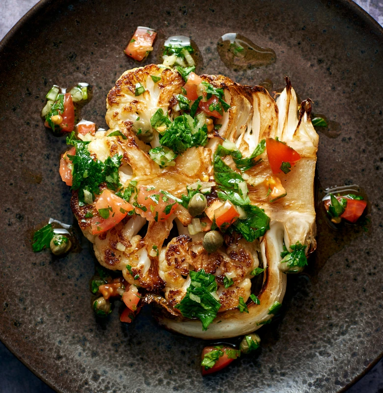 Golden-brown cauliflower steak with parsley on a plate.