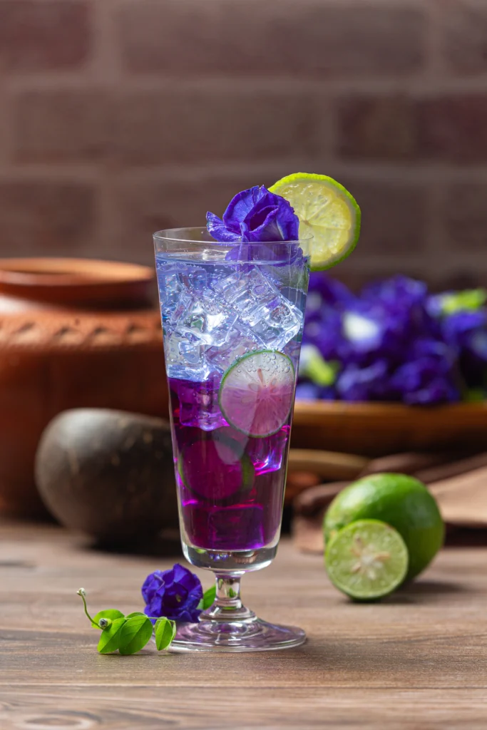 Icy lavender spritz with butterfly pea flower and lime on white wooden background.