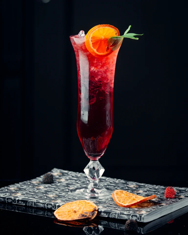 A tall champagne flute filled with deep ruby-red Kir Royal, garnished with a lemon twist against a dark textured backdrop.