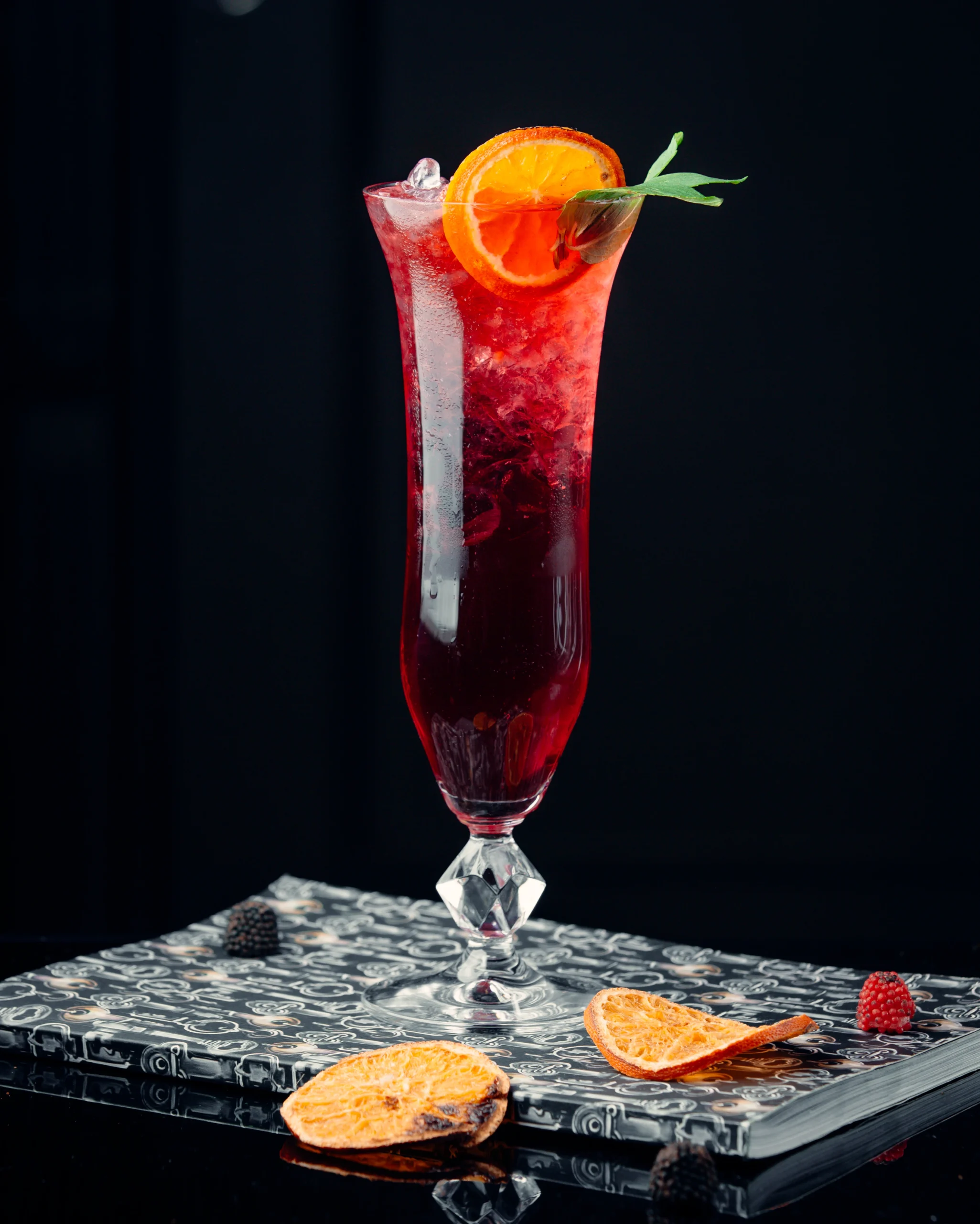 A tall champagne flute filled with deep ruby-red Kir Royal, garnished with a lemon twist against a dark textured backdrop.
