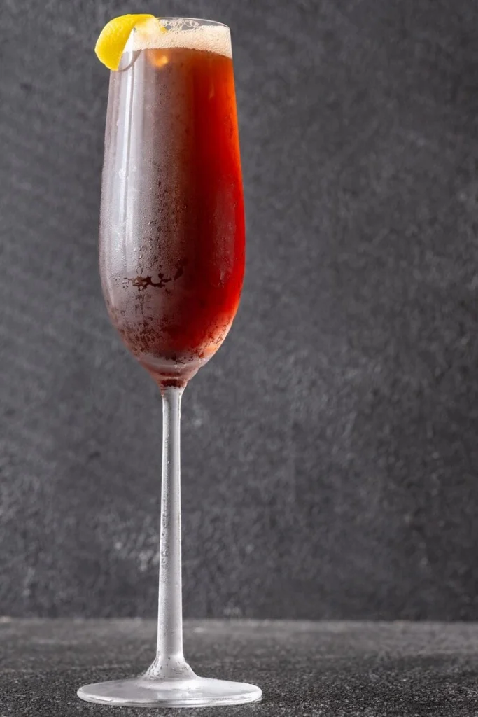 Dark red Kir Royal cocktail with citrus garnish in a tall glass.