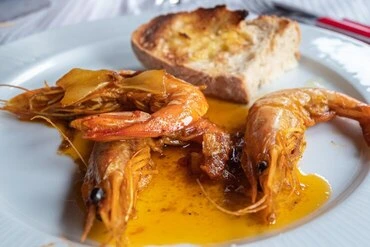 Spanish Gambas al Ajillo served with garlic oil and crusty bread on a white plate.