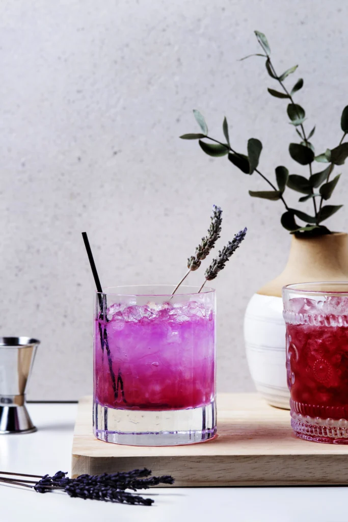 Tall glass of lavender spritz with butterfly pea flower and sliced lime.