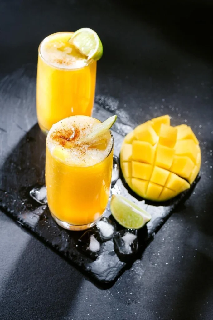 Icy mango caipirinha cocktail with kiwi slice and greenery, served on a wooden tray.
