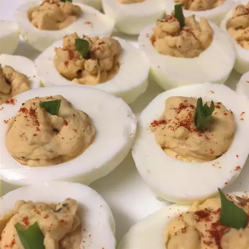 Creamy devilled egg potato salad topped with paprika and herbs in a white bowl.