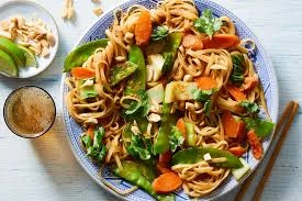 Colorful Chicken & Broccoli Rice Noodle Stir Fry served on a blue plate with chopsticks, featuring vegetables like carrots, snap peas, and garnished with peanuts.