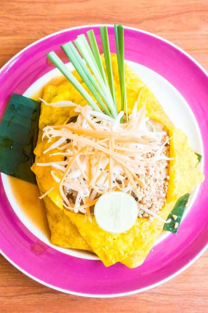 Traditional Khmer Nom Banh Chok served with herbs, banana blossom, and green fish sauce in a ceramic bowl.