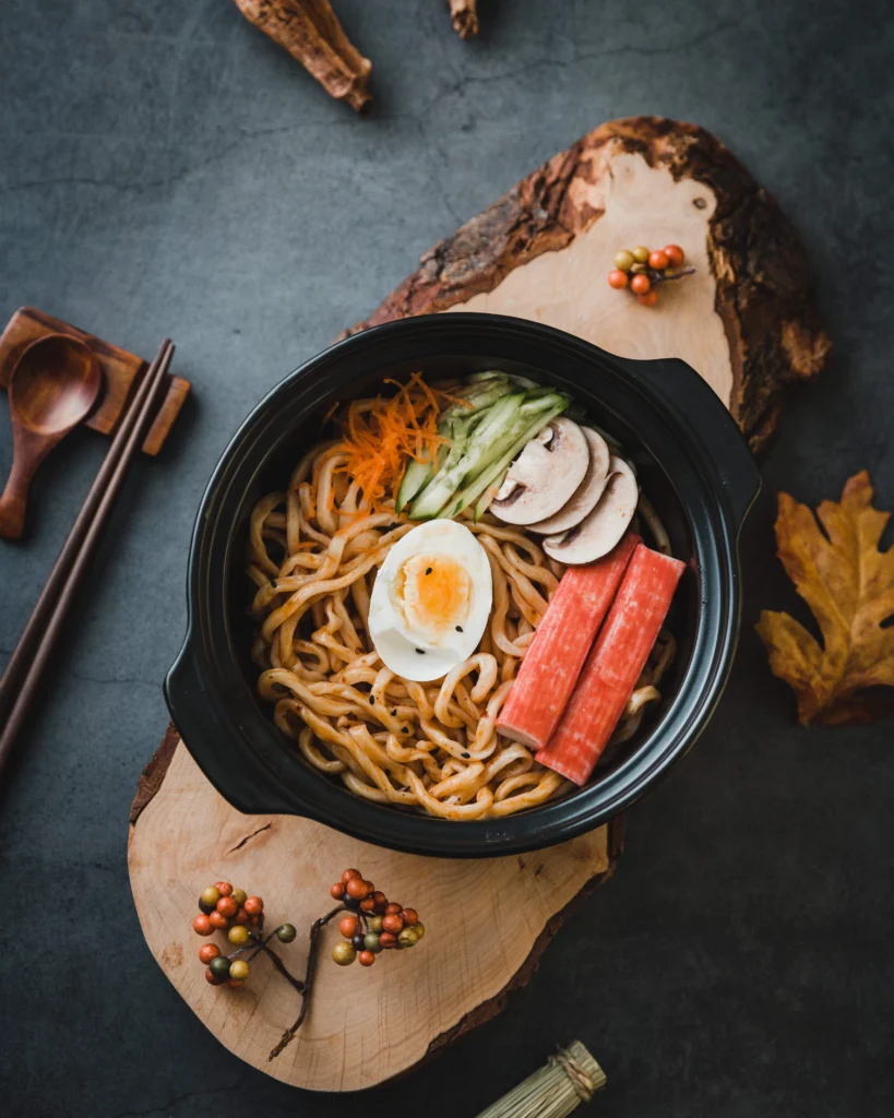 A close-up of a ramen bowl with tofu, egg, kimchi, seaweed, sprouts, and noodles on a white wooden background.