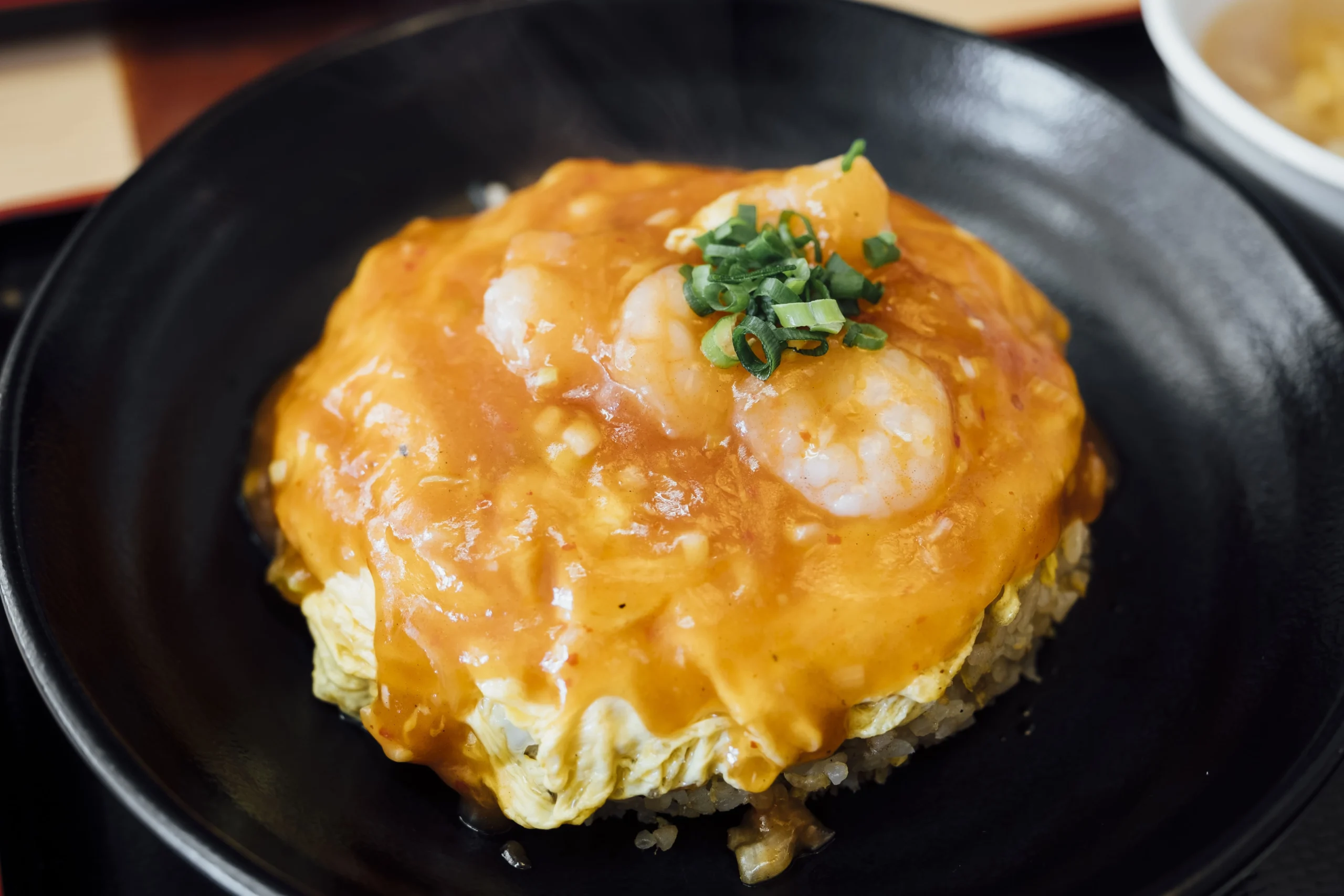 Japanese-style egg rice (Tamago Kake Gohan) with shrimp and savory sauce in a black bowl