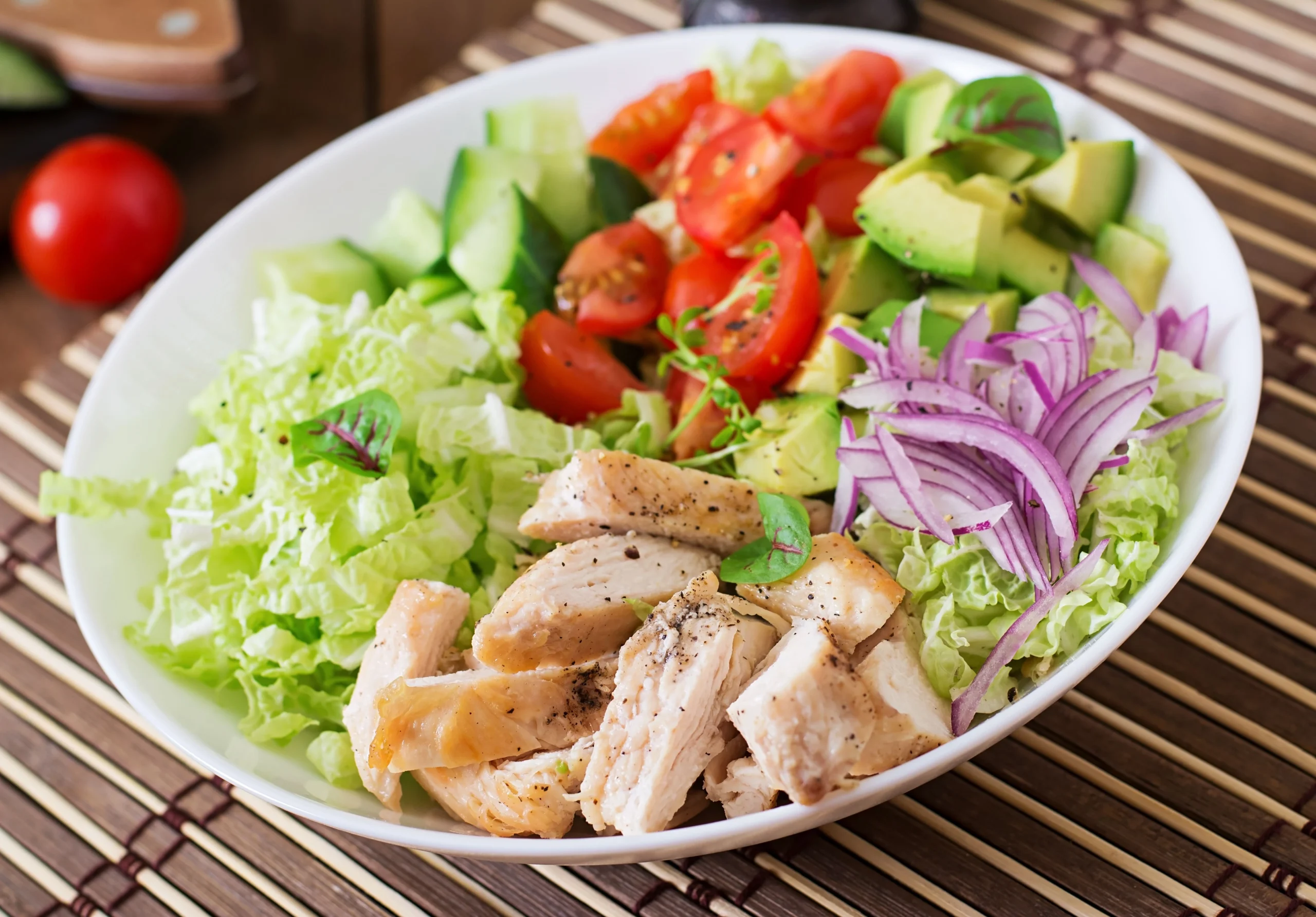 Classic Cobb Salad with grilled chicken, crispy bacon, avocado, eggs, blue cheese, and fresh vegetables on a large white plate.