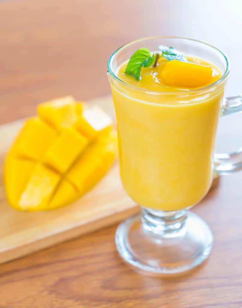 Frosty mango lassi with black specks, served with a straw and tropical garnish on a sunny table.