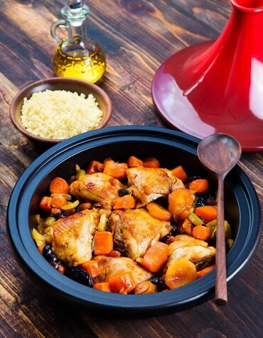 Festive chicken apricot stew with carrots, peas, and bay leaf in a white bowl, surrounded by pinecones and gold ornaments.