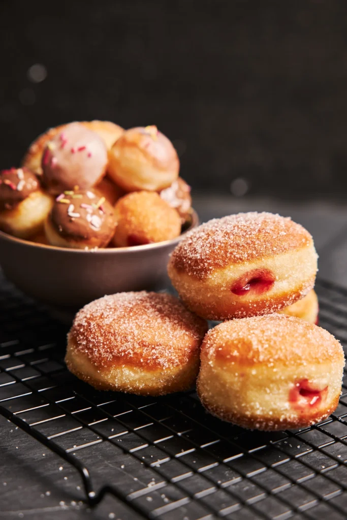 Close view of sugar-dusted Bolinhos de Chuva with soft golden texture and fruit jam inside.