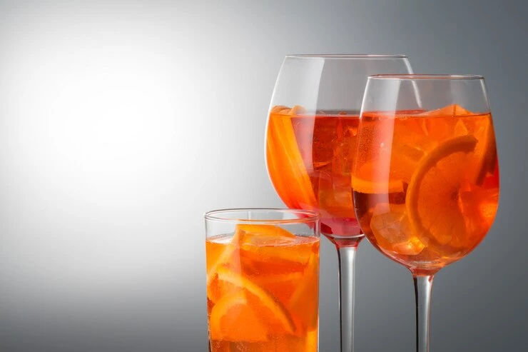 Chilled Campari Orange cocktail with orange slice and mint, glowing in sunlight on a patio table.
