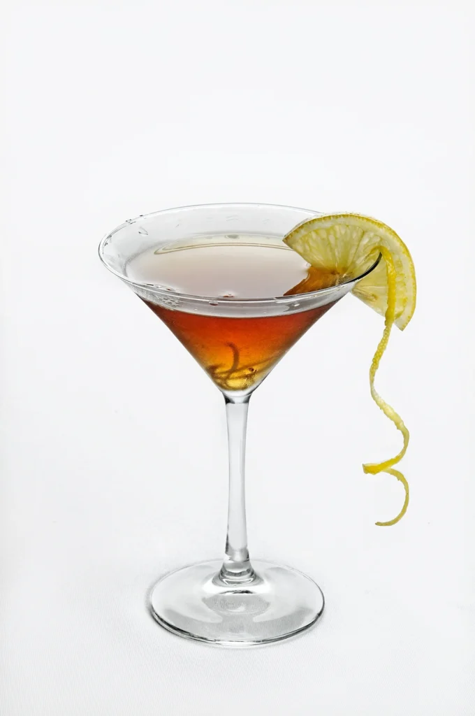 A classic Manhattan cocktail served in a martini glass, garnished with a lemon twist on the rim.