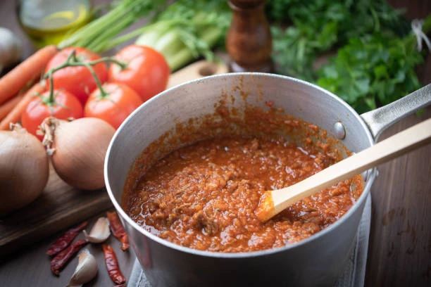 A steaming bowl of pasta with thick tomato and meat ragu sauce on a rustic tabletop.
