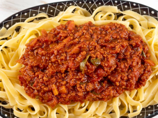 Forkful of pasta twirled above a bowl of homemade ragu sauce on a wooden table.
