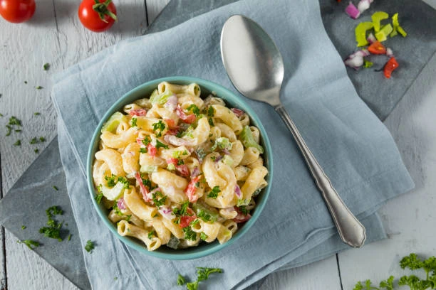 Macaroni salad topped with chopped chives in a floral serving bowl