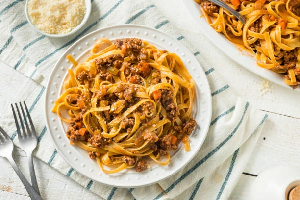 Rich red ragu sauce with ground meat and chickpeas, served over thick spaghetti in a rustic bowl.
