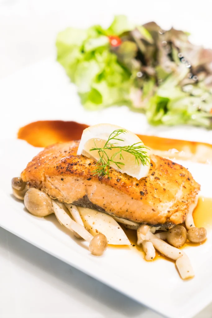 Wild Alaskan Salmon fillet with yellow sauce, green mash, and fresh garnish on a white plate.