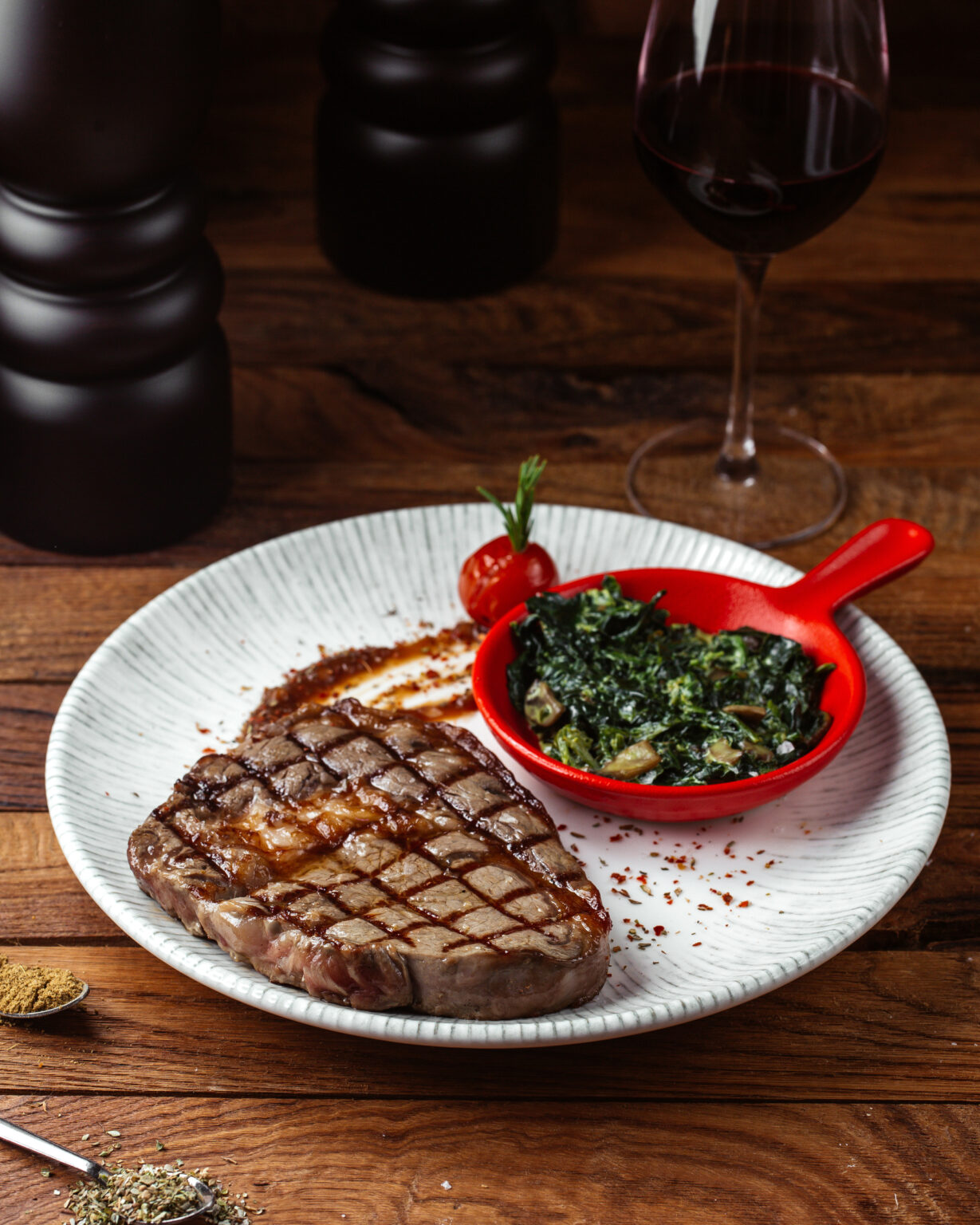 Juicy Grilled Ribeye Steak served with sautéed greens and a glass of red wine on a rustic wooden table.